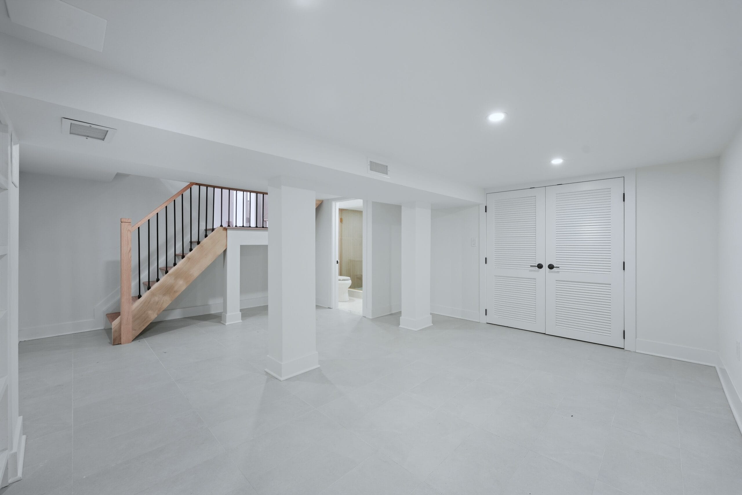 Finished lower level with a new oak-and-iron staircase, louvered storage doors, and porcelain tile floors
