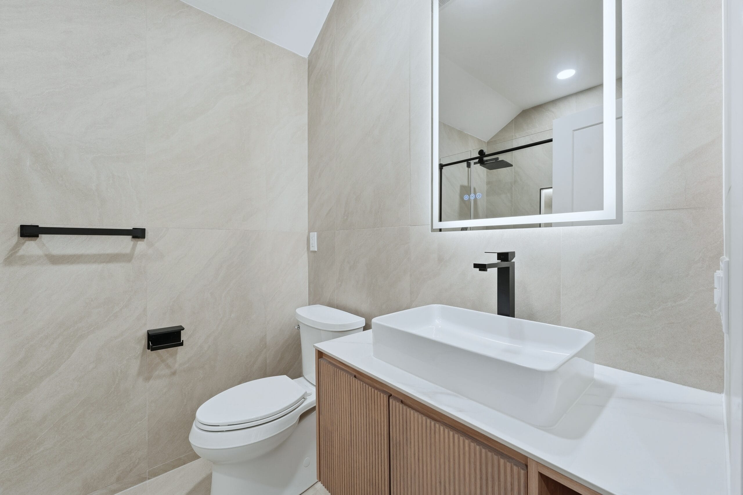 Bathroom finished in stone-look tile with a frameless glass shower, vessel sink, and matte-black fixtures