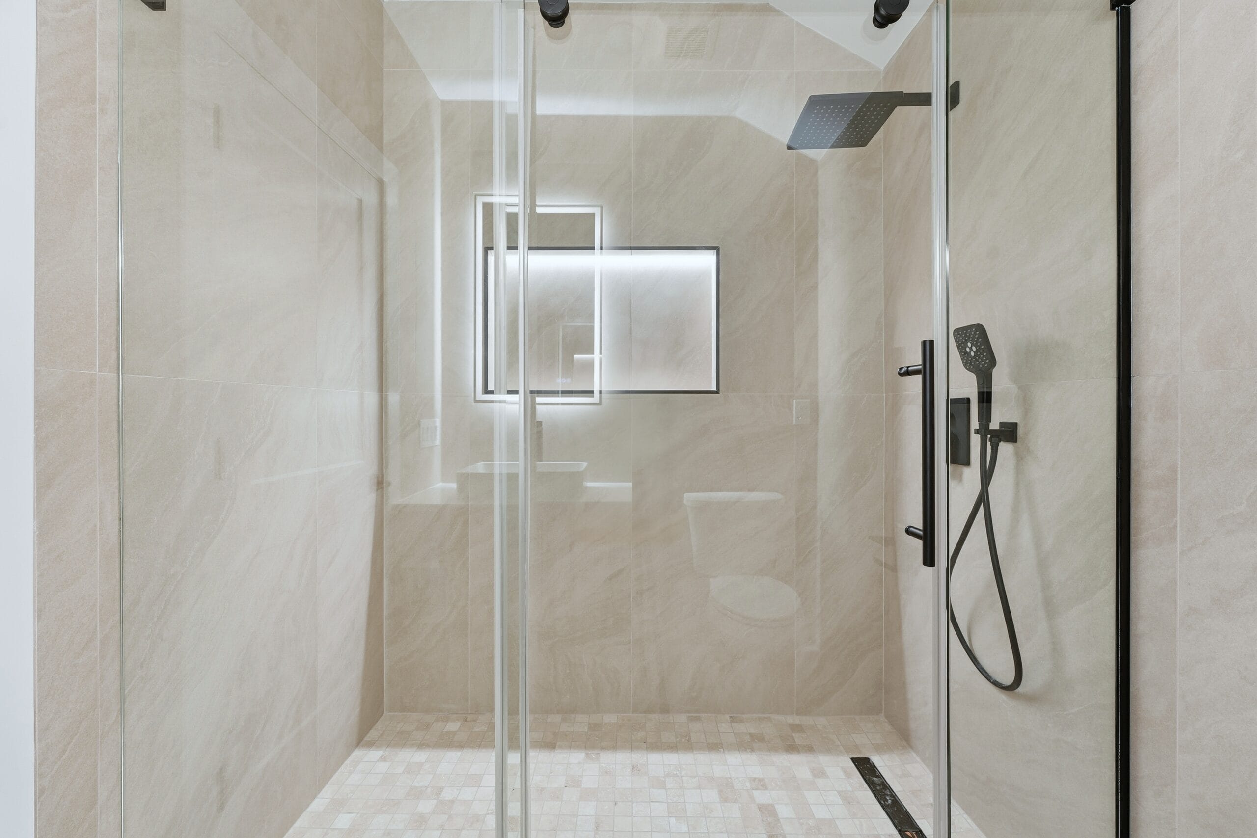 Walk-in shower clad in beige stone-look porcelain with dual matte-black rainfall heads and a mosaic floor