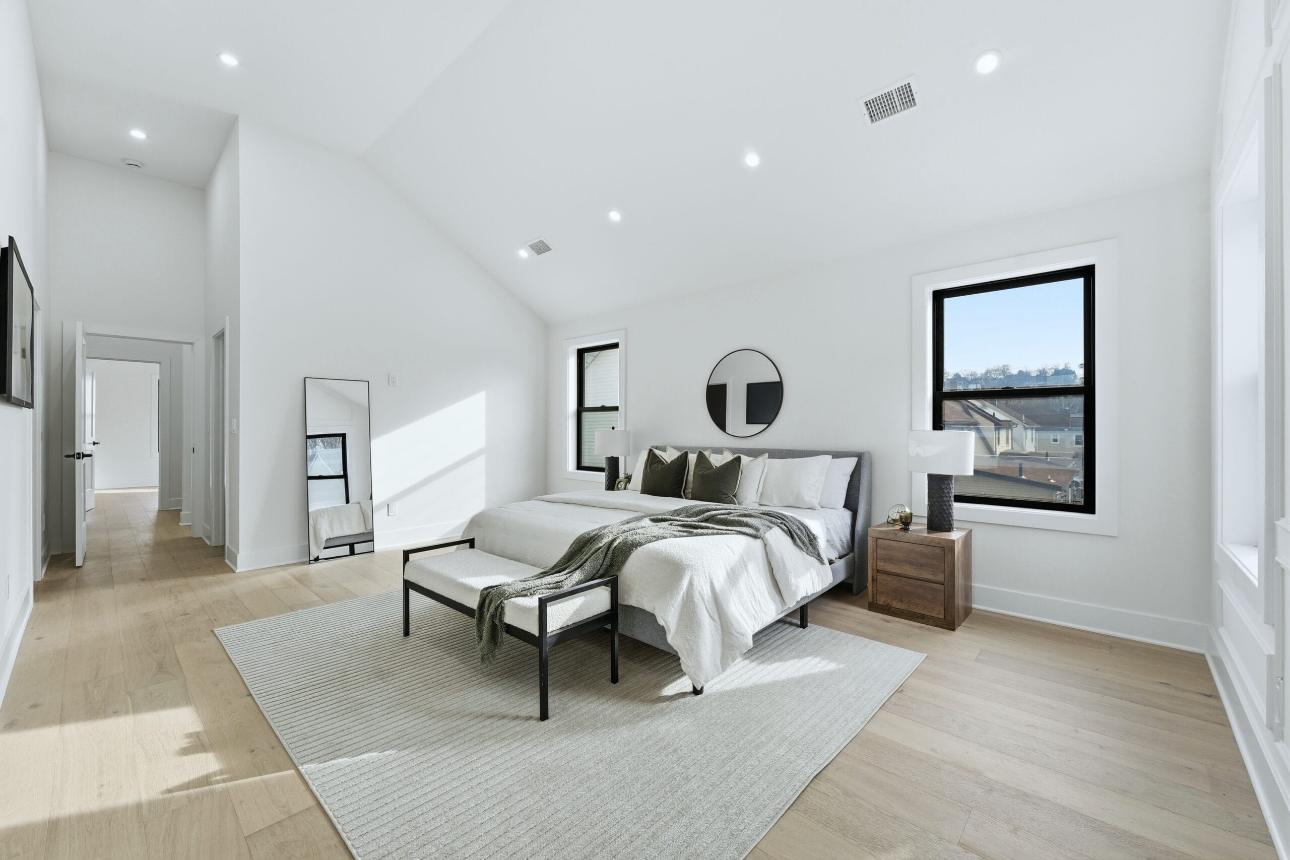 Primary bedroom with a vaulted ceiling, large black-framed windows, and warm staged furnishings