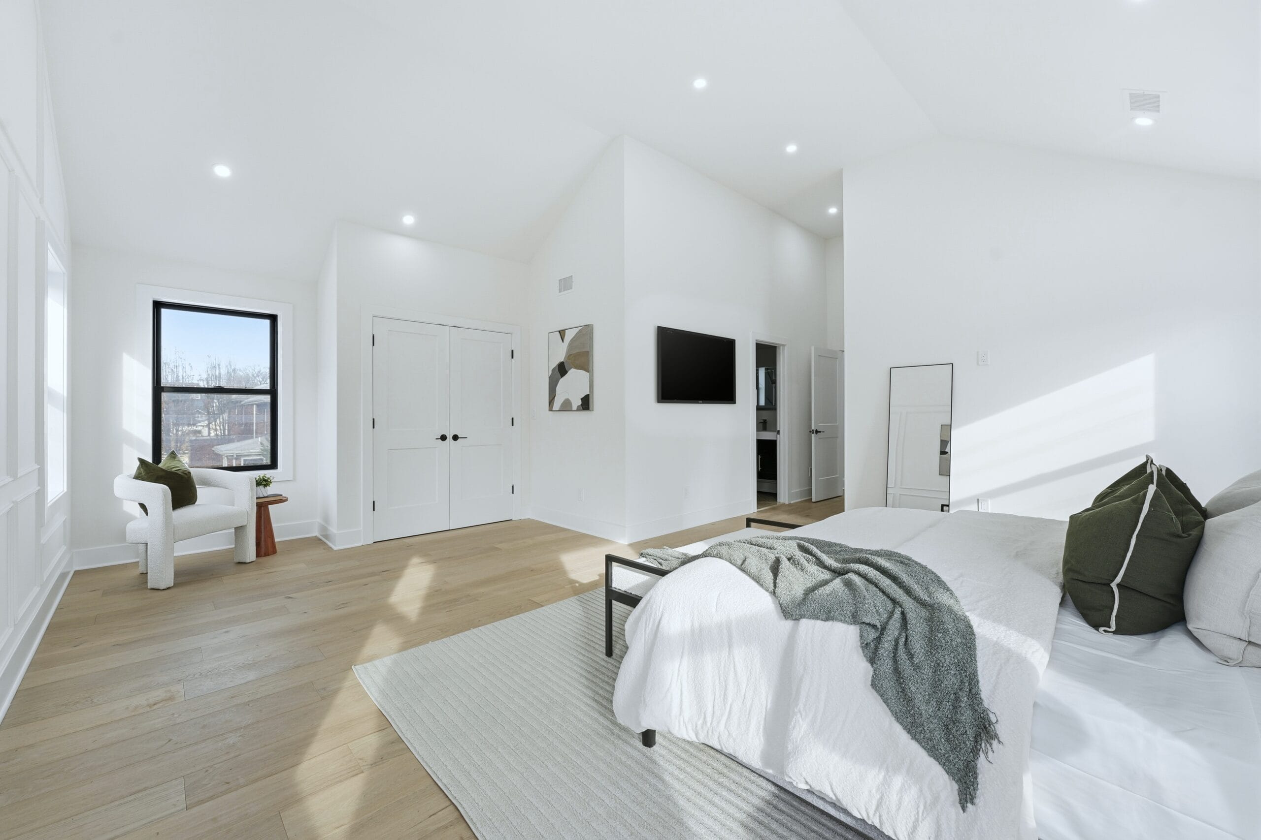 Vaulted primary bedroom with white oak floors, a sculptural bouclé chair, and abundant natural light