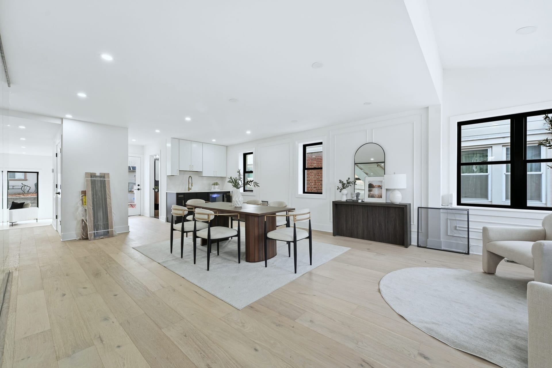 Open-plan dining and kitchen with white oak floors, a walnut table, and black-framed windows