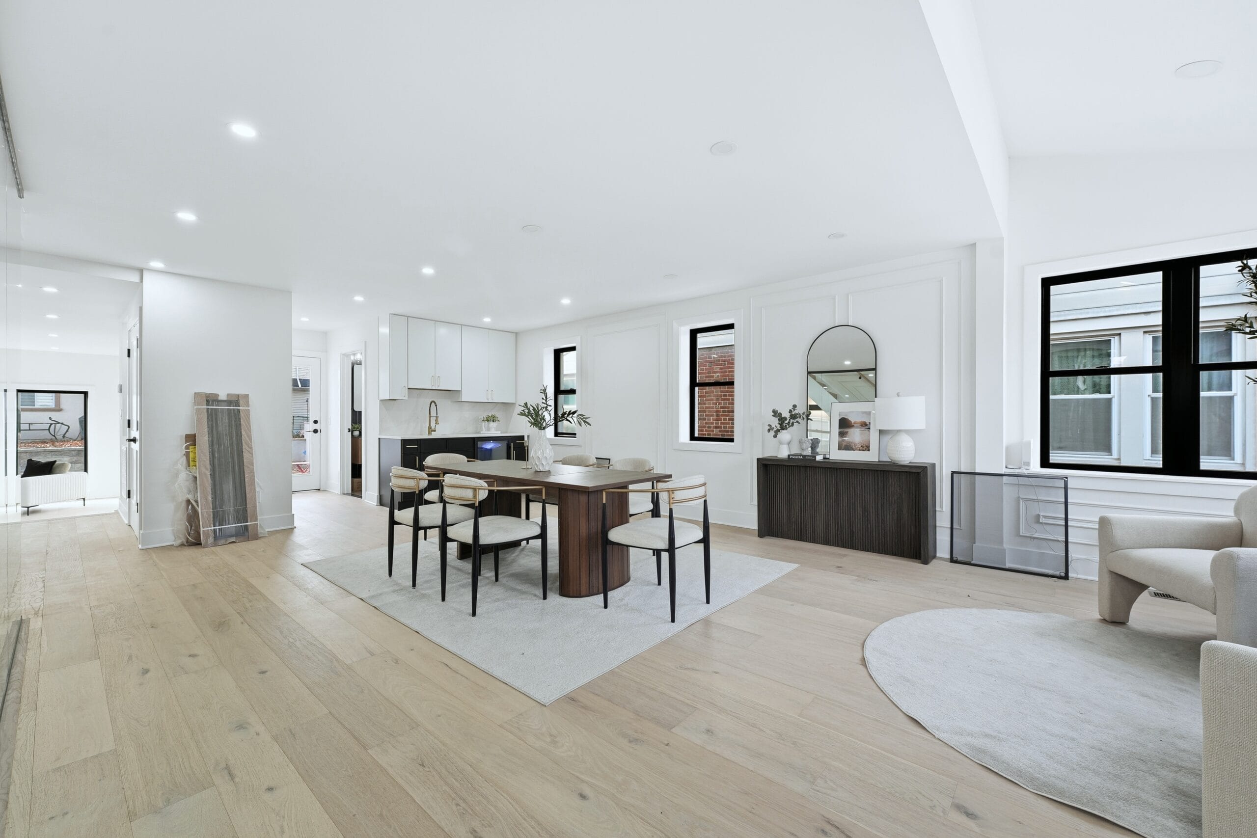 Open-plan dining and kitchen with white oak floors, a walnut table, and black-framed windows