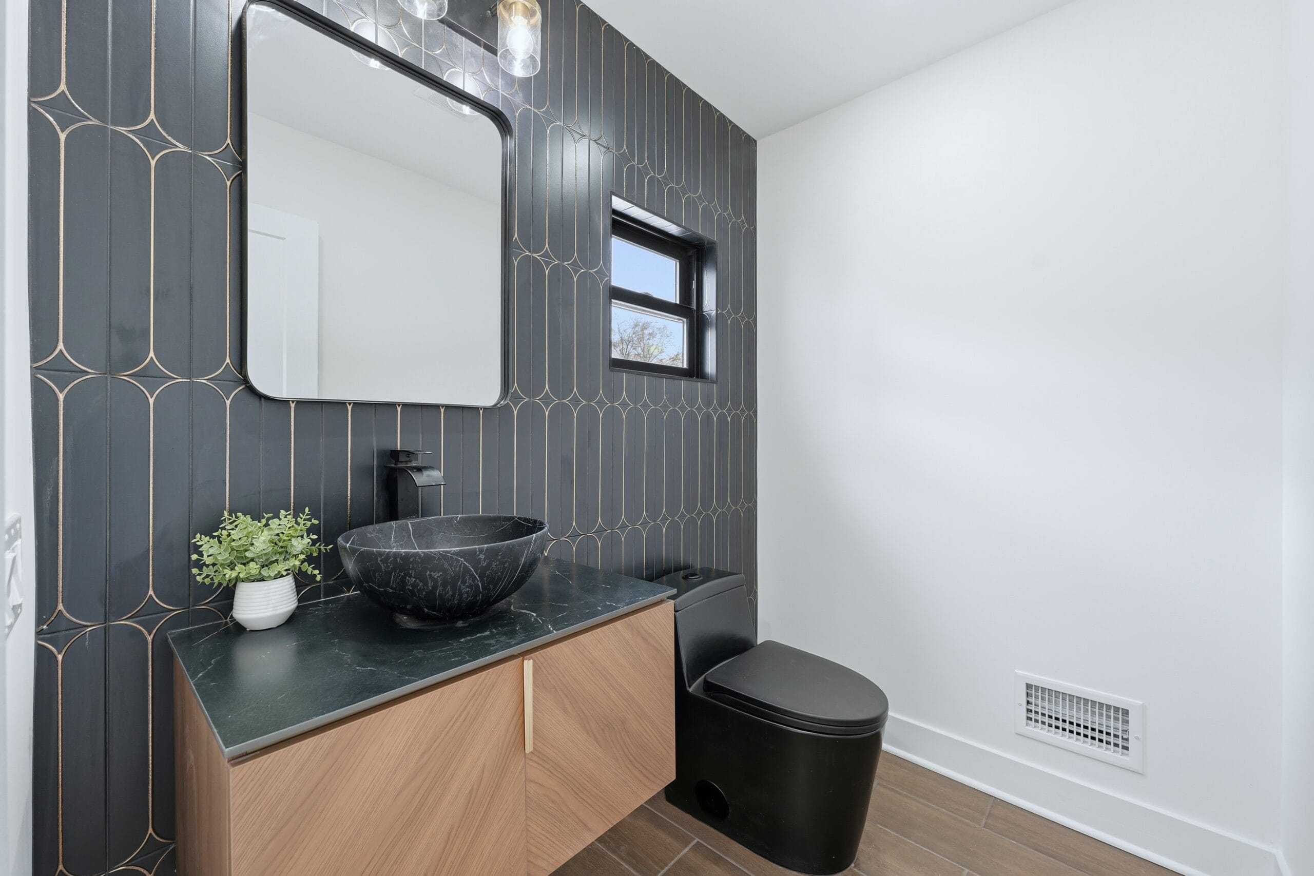 Powder room with deep green and gold art-deco wall tile, a black marble vessel sink, and a fluted oak vanity