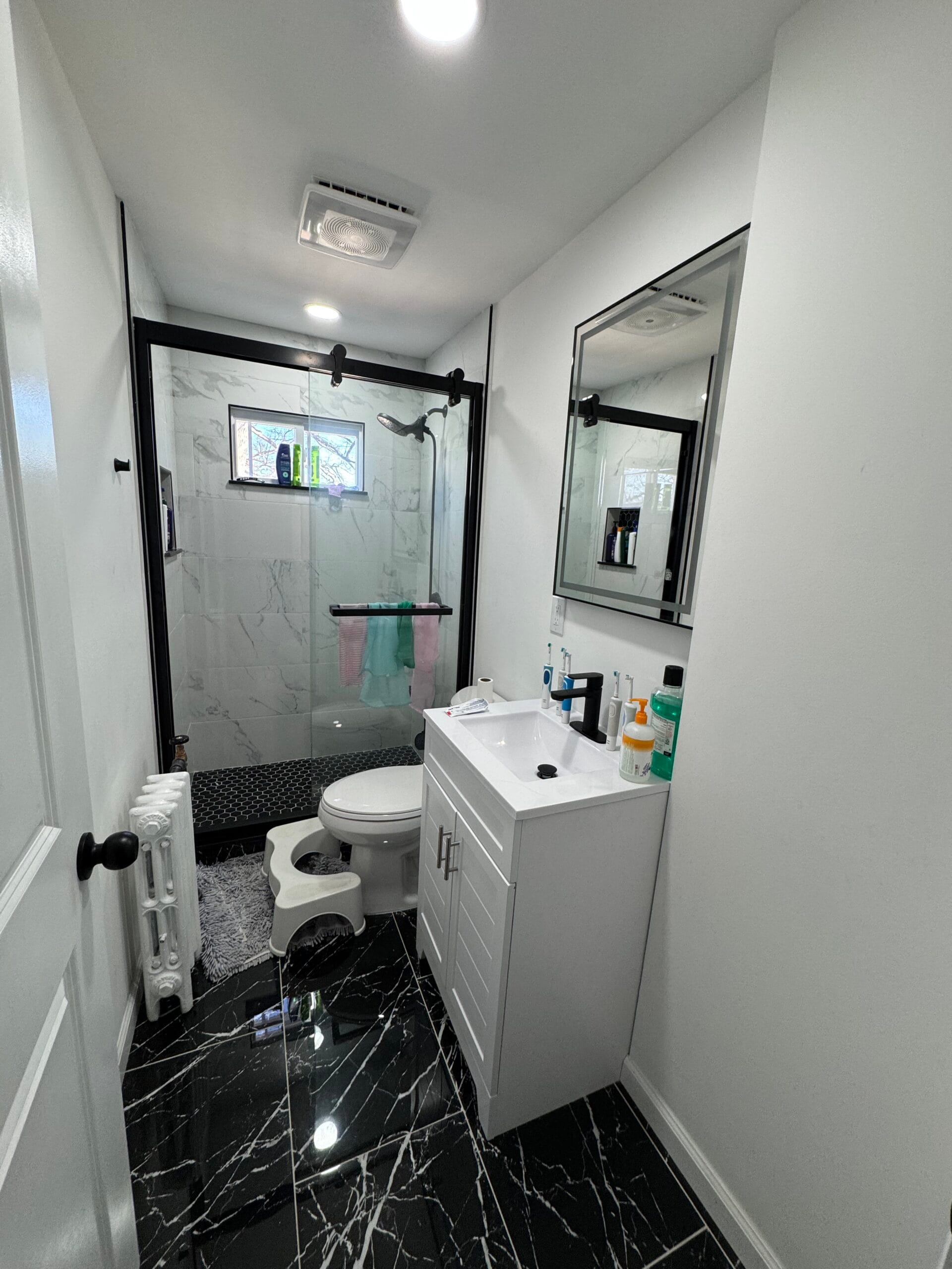 Renovated Englewood bathroom with grey marble-look tile, a glass shower, and a modern white vanity