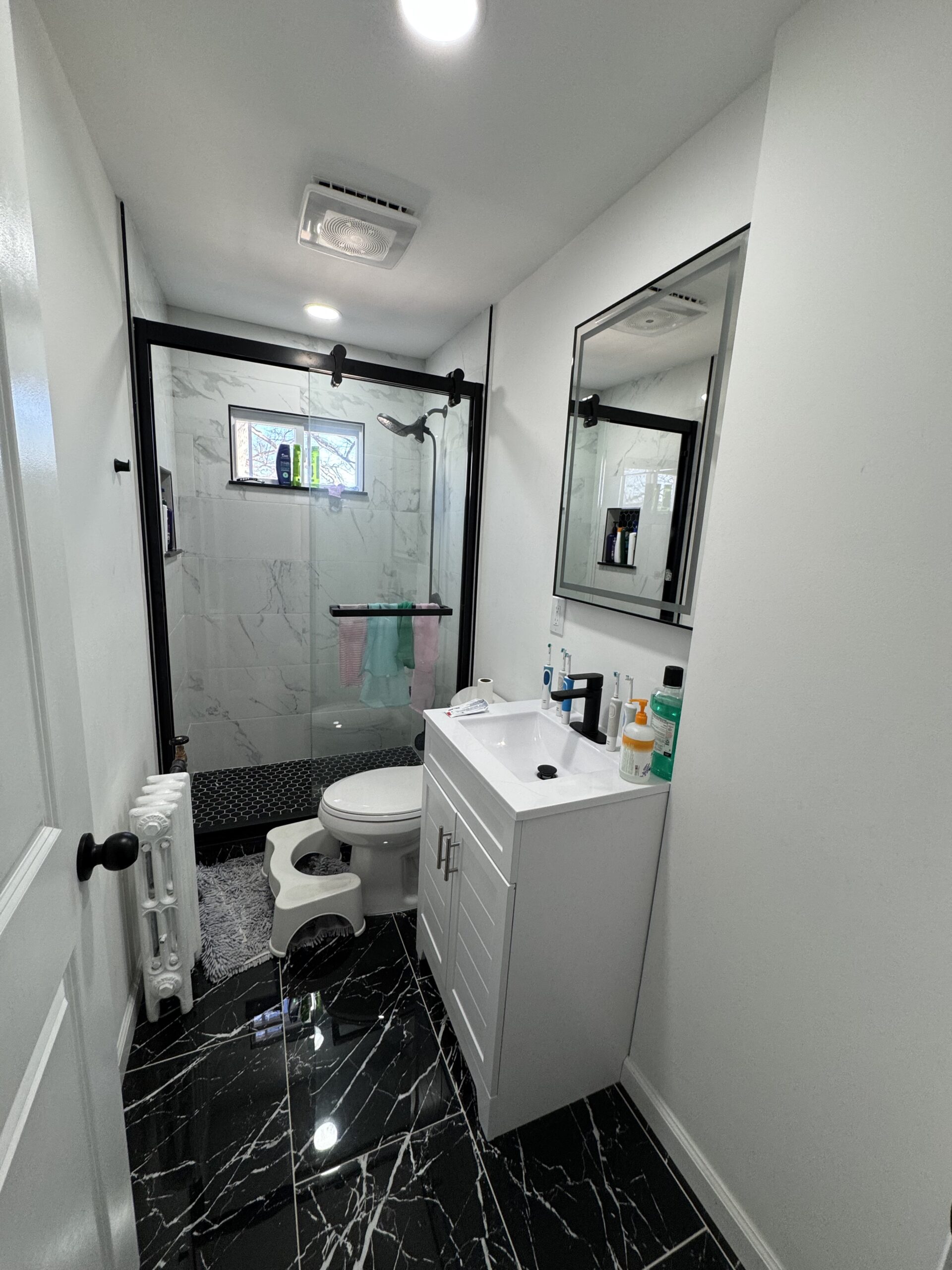 Renovated Englewood bathroom with grey marble-look tile, a glass shower, and a modern white vanity